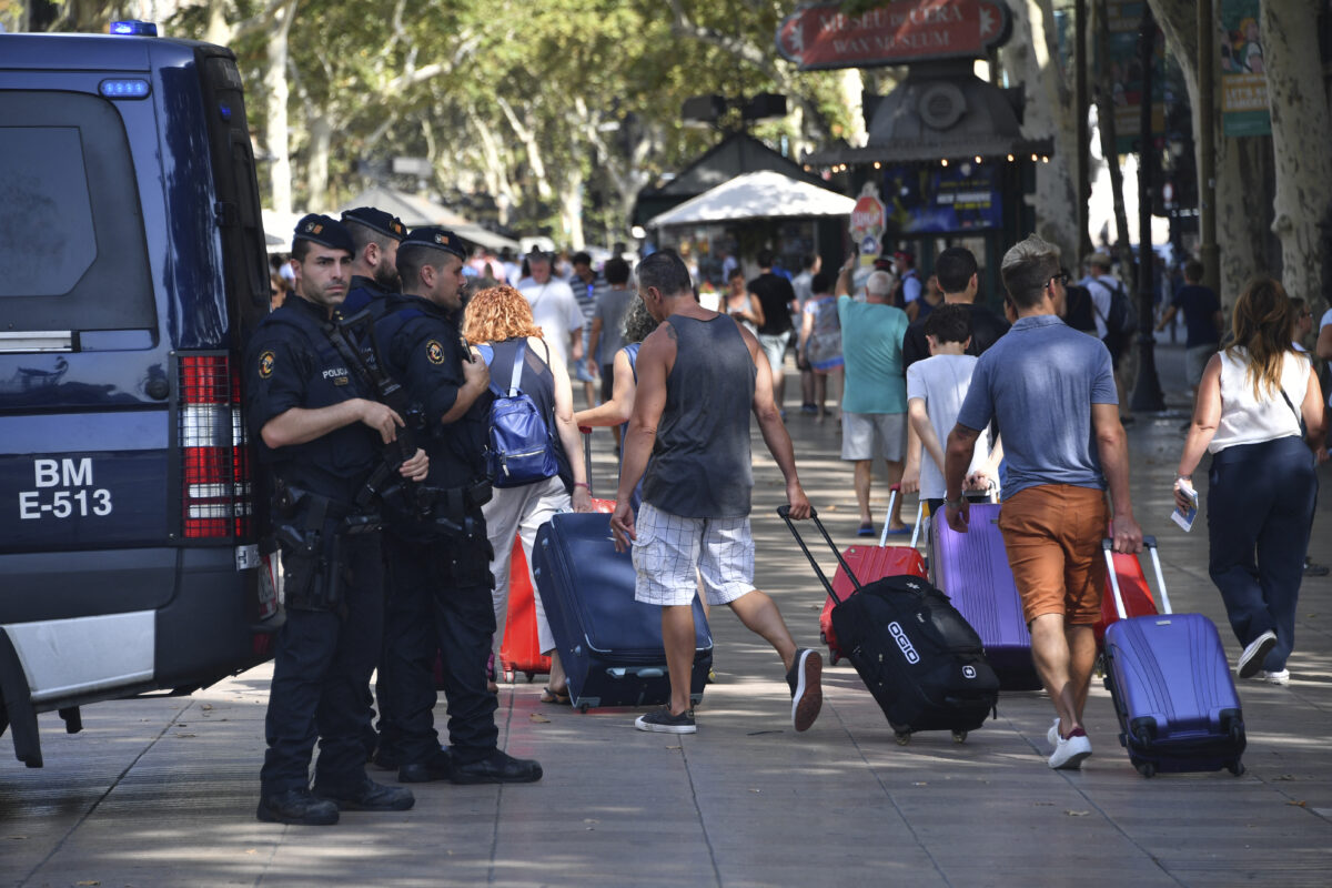 Spanish policemen stand guard as tourists pass by with their suitcases on the Rambla boulevard on August 18, 2017 a day after a van ploughed into the crowd, killing 13 persons and injuring over 100 on the Rambla in Barcelona. Drivers have ploughed on August 17, 2017 into pedestrians in two quick-succession, separate attacks in Barcelona and another popular Spanish seaside city, leaving 13 people dead and injuring more than 100 others. In the first incident, which was claimed by the Islamic State group, a white van sped into a street packed full of tourists in central Barcelona on Thursday afternoon, knocking people out of the way and killing 13 in a scene of chaos and horror. Some eight hours later in Cambrils, a city 120 kilometres south of Barcelona, an Audi A3 car rammed into pedestrians, injuring six civilians -- one of them critical -- and a police officer, authorities said. (Photo by Pascal GUYOT / AFP)