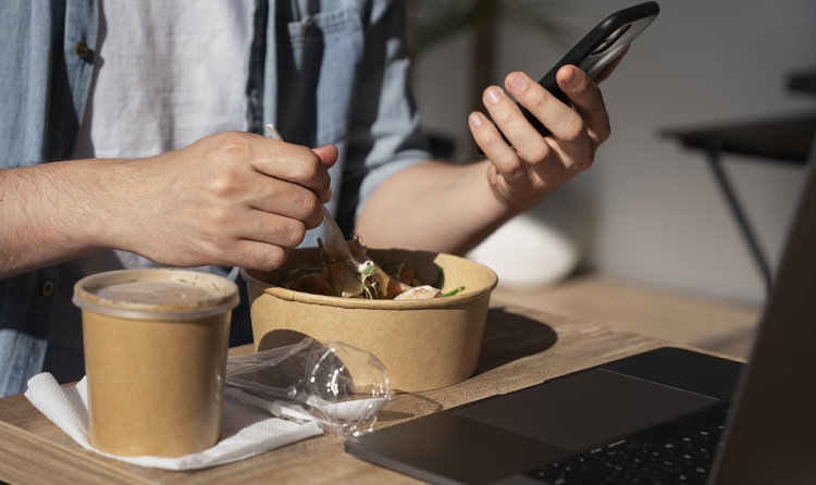 Man enjoying takeaway food and using smartphone (Font: freepik)